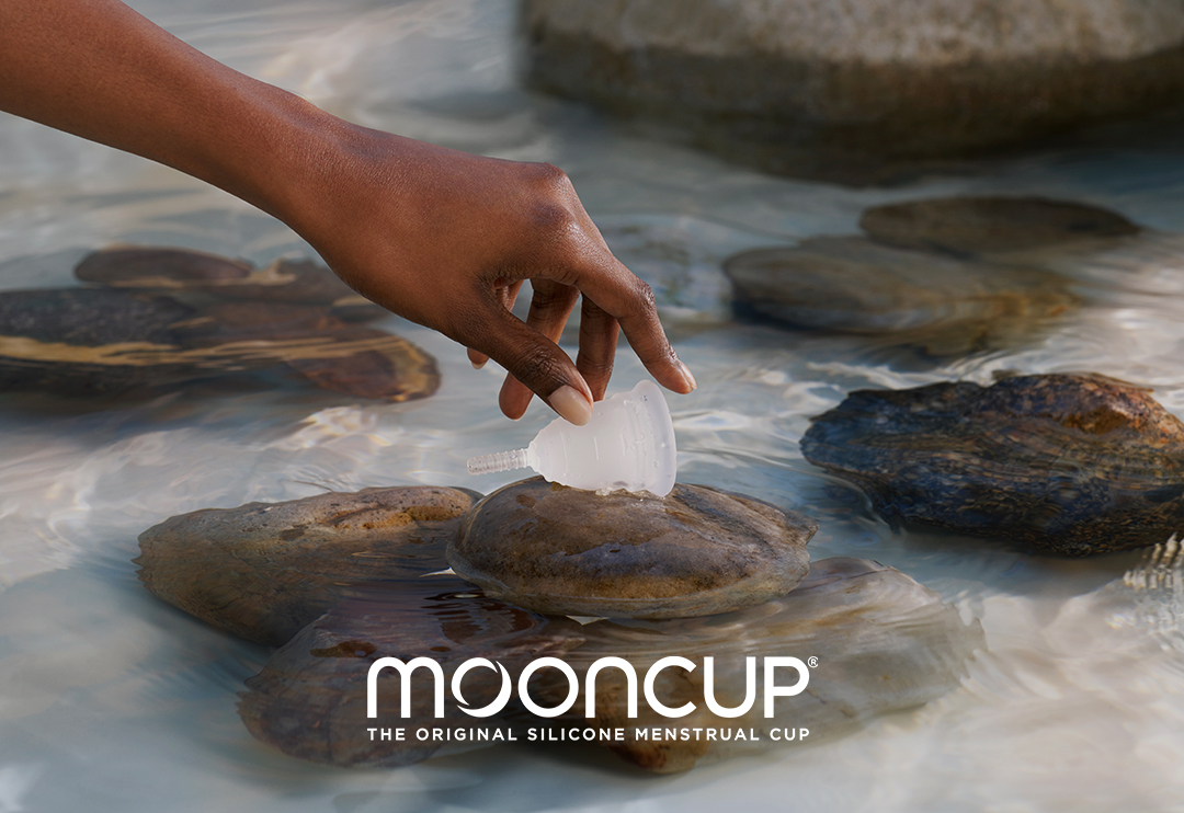 Someone putting their hand on a mooncup that's on a rock in water