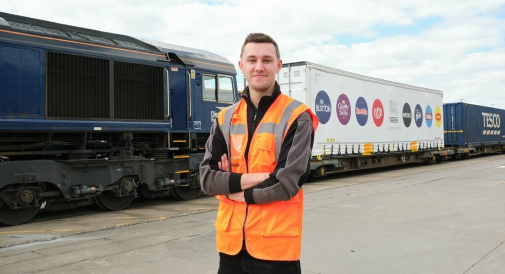 Person in orange vis coat standing in front of Nestlé double-stacked rail train