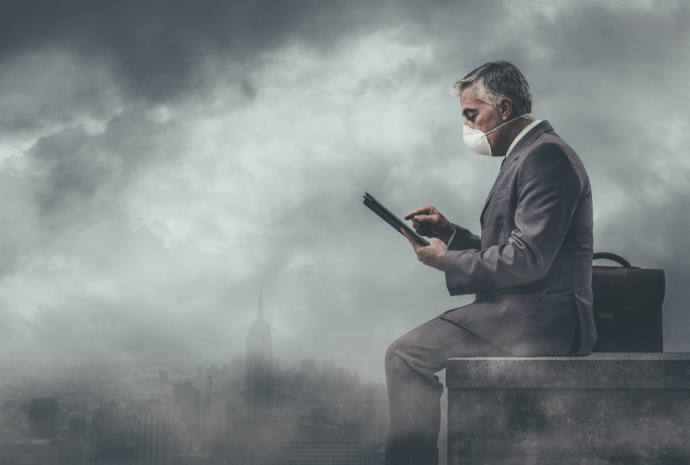 Businessman sitting on a rooftop in a polluted city and using a tablet: environmental pollution, air quality and business concept