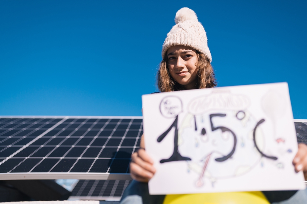 Teenage girl protests next to solar panels with a painted sign calling for preventing the earth's temperature from rising by 1.5 degrees Celsius. Awareness of the new generations. Climate summit IEA
