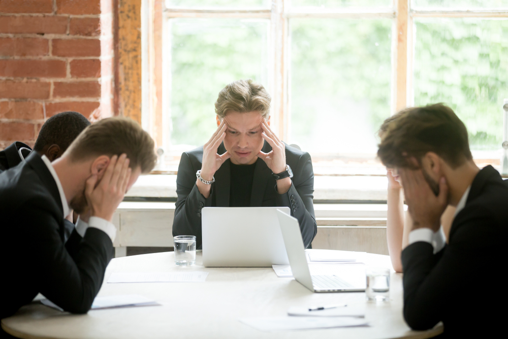 Stressed boss and executives searching problem solution at meeting, partners holding heads in hands depressed by failure bad news, feeling desperate about company bankruptcy or financial crisis