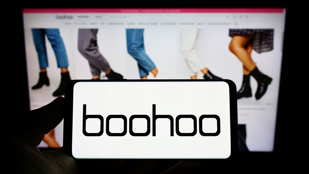 Person holding cellphone with logo of British fashion company Boohoo Group plc on screen in front of business webpage. Focus on phone display. Unmodified photo.