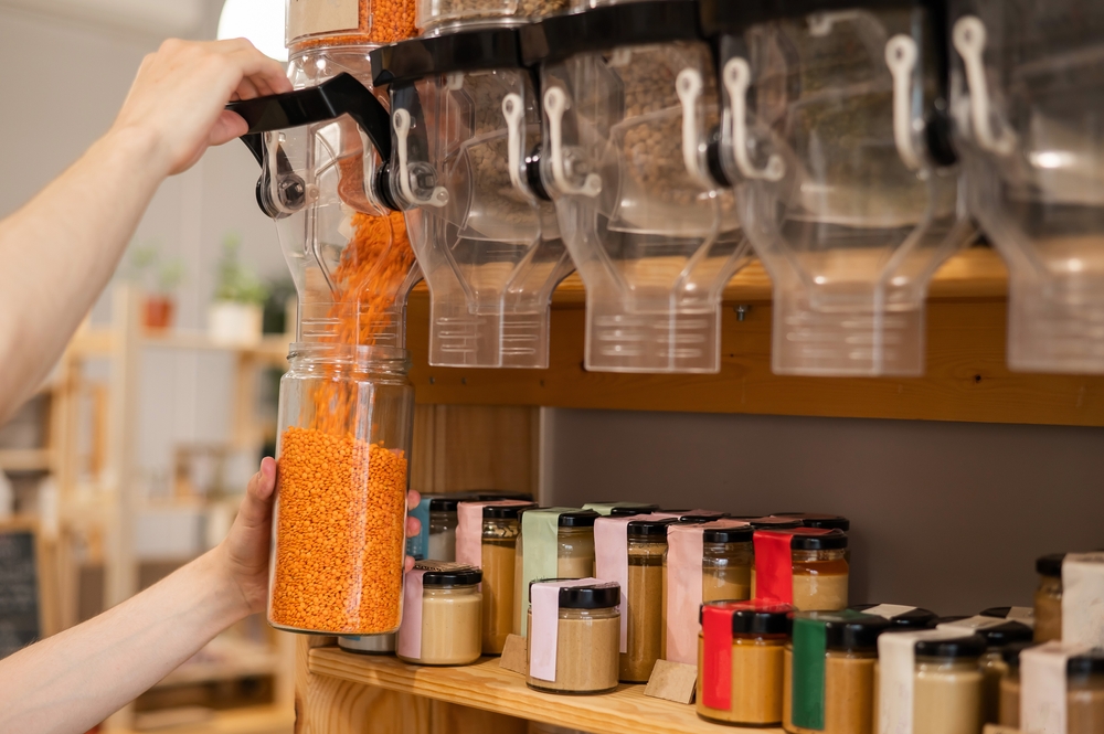 A man fills a jar with red lentils. Selling bulk goods by weight in an eco store. Trade concept without plastic packaging. returnable packaging