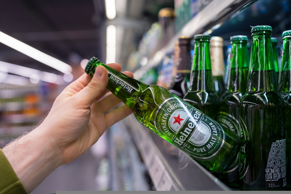 Buyer takes Heineken bottle beer from the shelves in the supermarket. Hand is holding Heineken beer. Minsk, Belarus - june, 2022